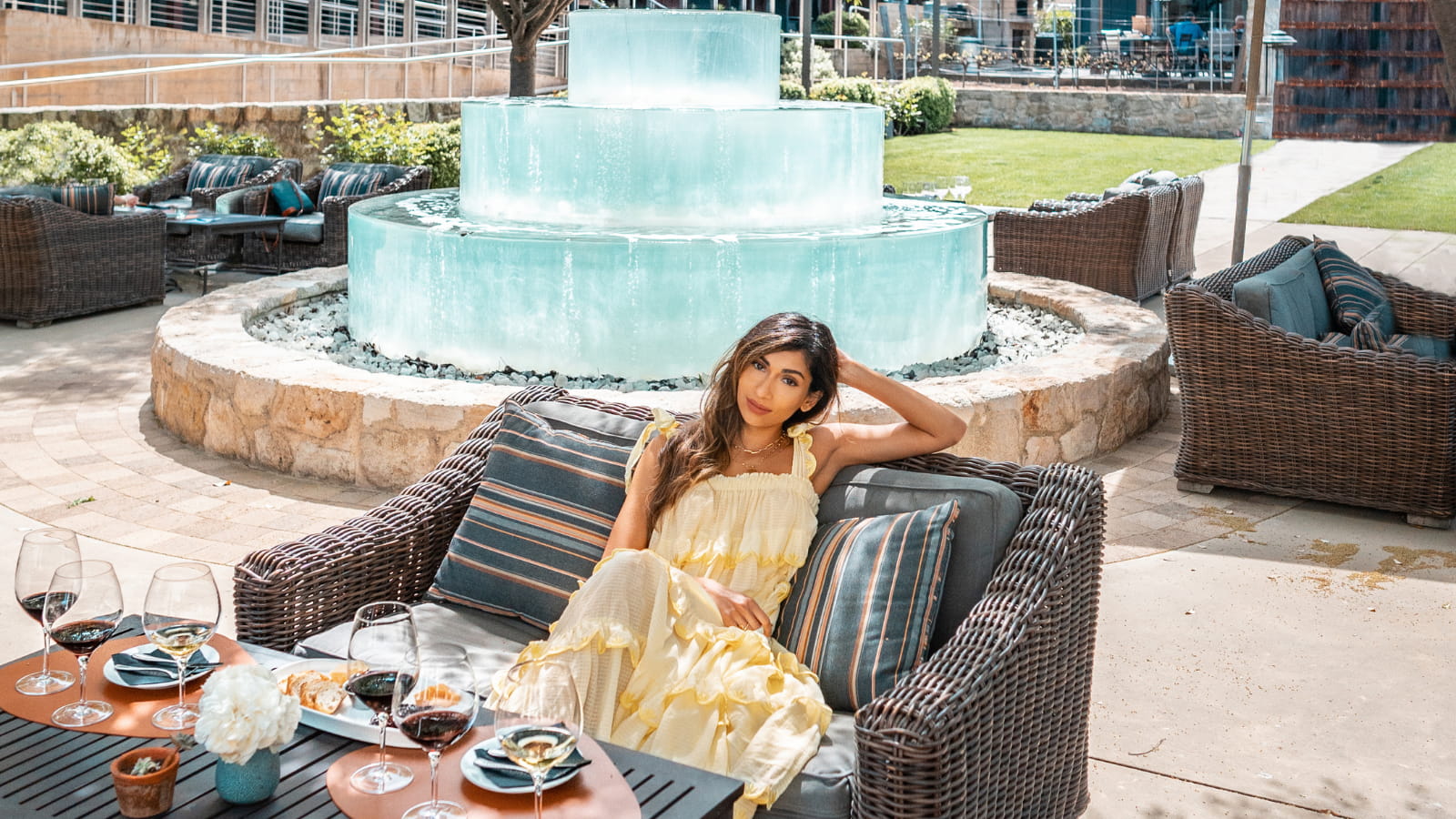 Woman relaxing by turquoise fountain with wine glasses.