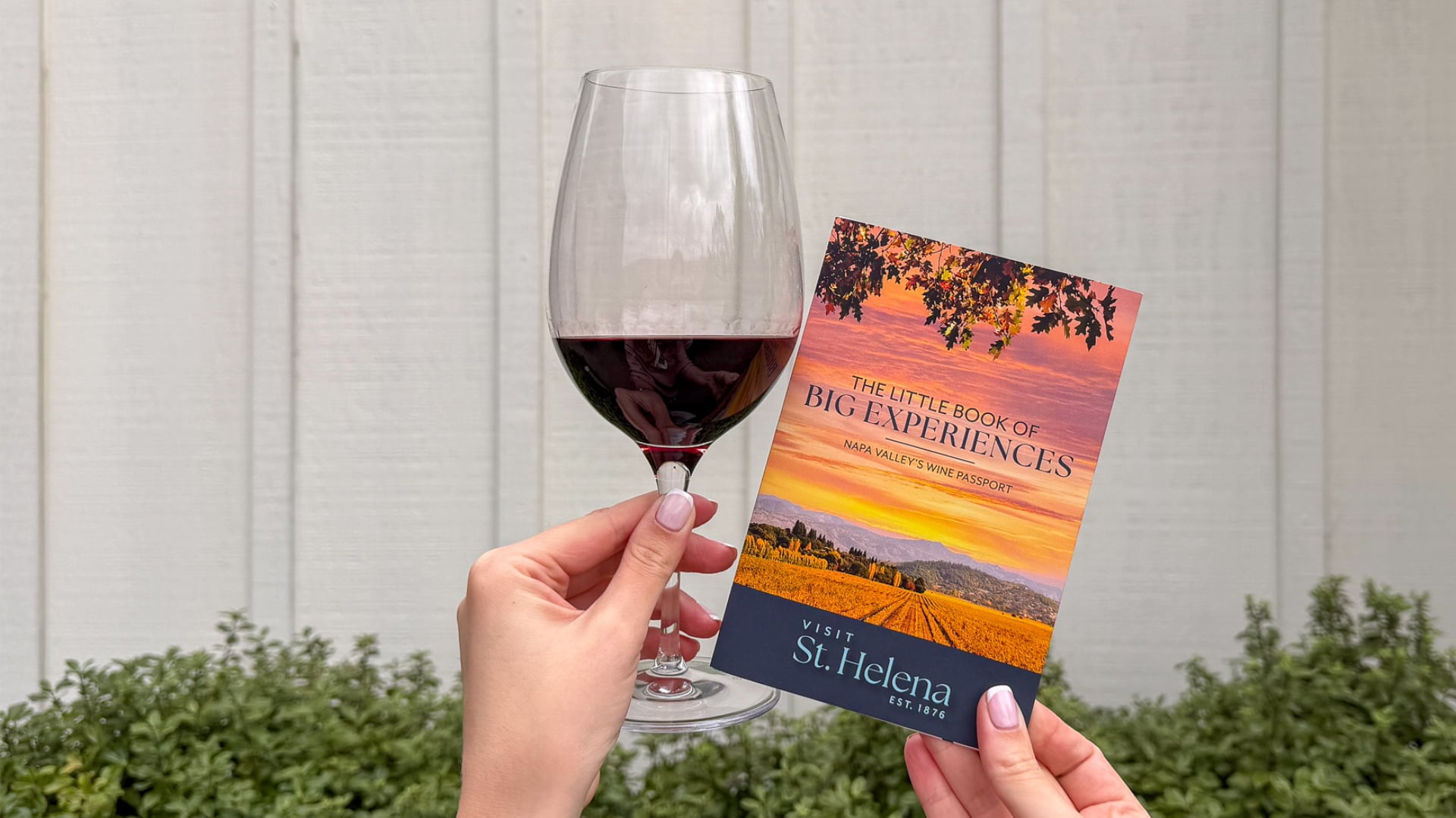 Hands hold red wine glass and St. Helena passport
