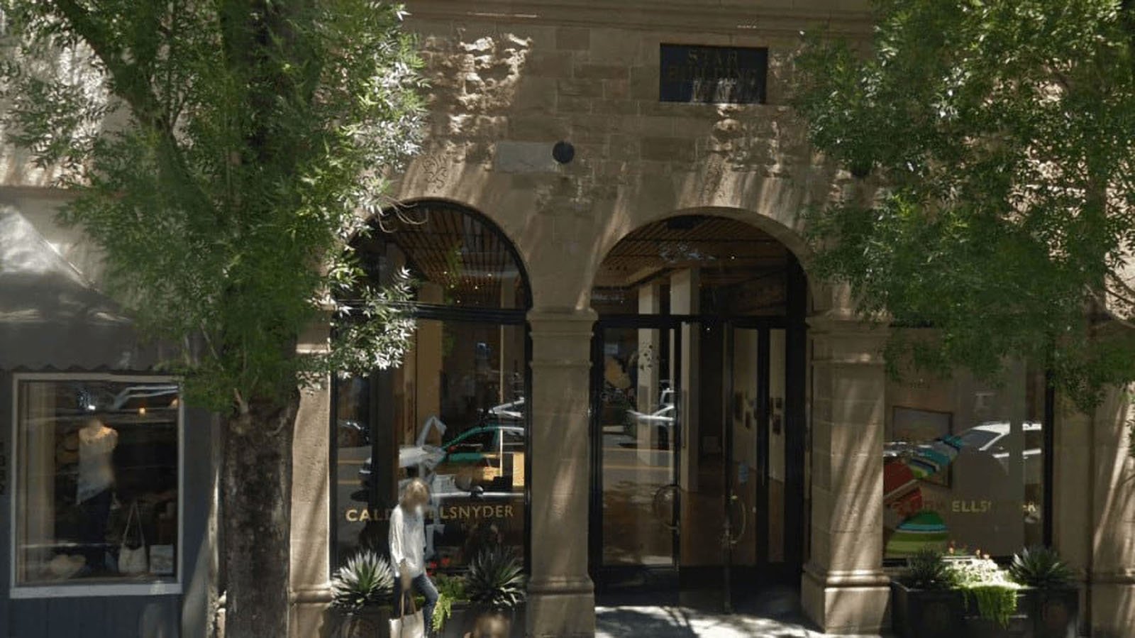Storefront with arched stone entrance and trees.