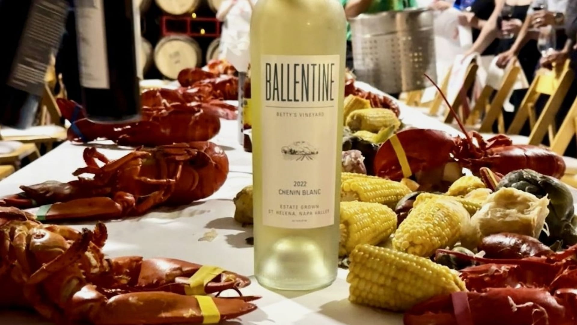 Wine bottle with lobsters and corn on table.