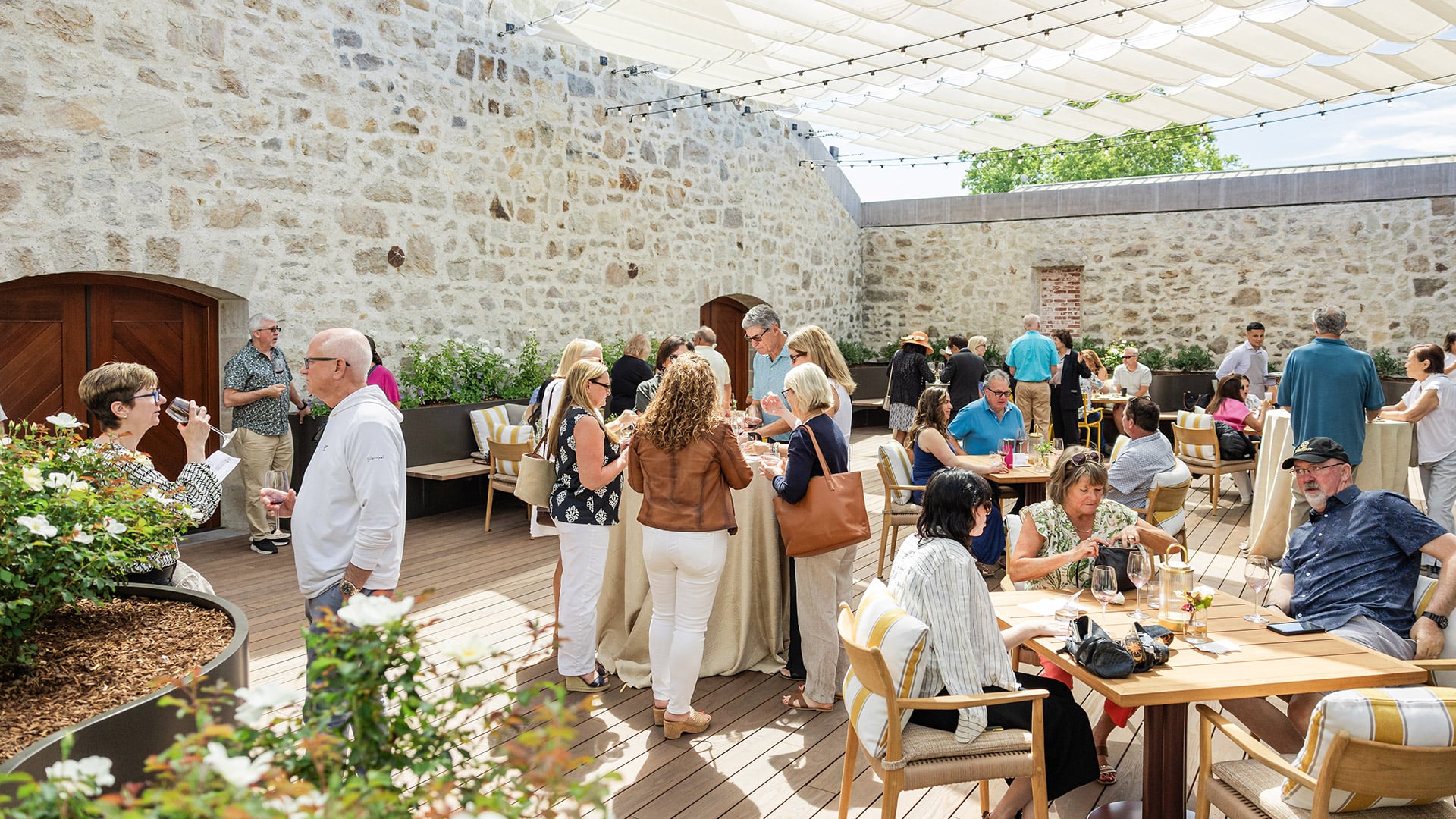 Guests socialize on a sunlit stone courtyard patio.