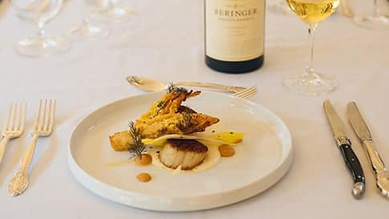 Gourmet dish with wine on white tablecloth.
