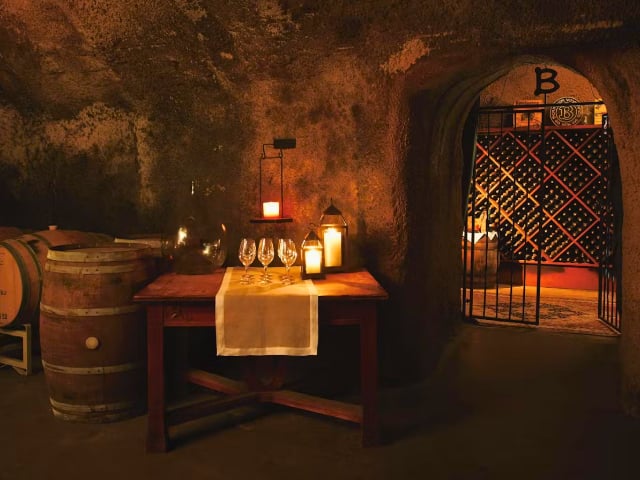 Candlelit wine cellar table beside barrels and wine rack