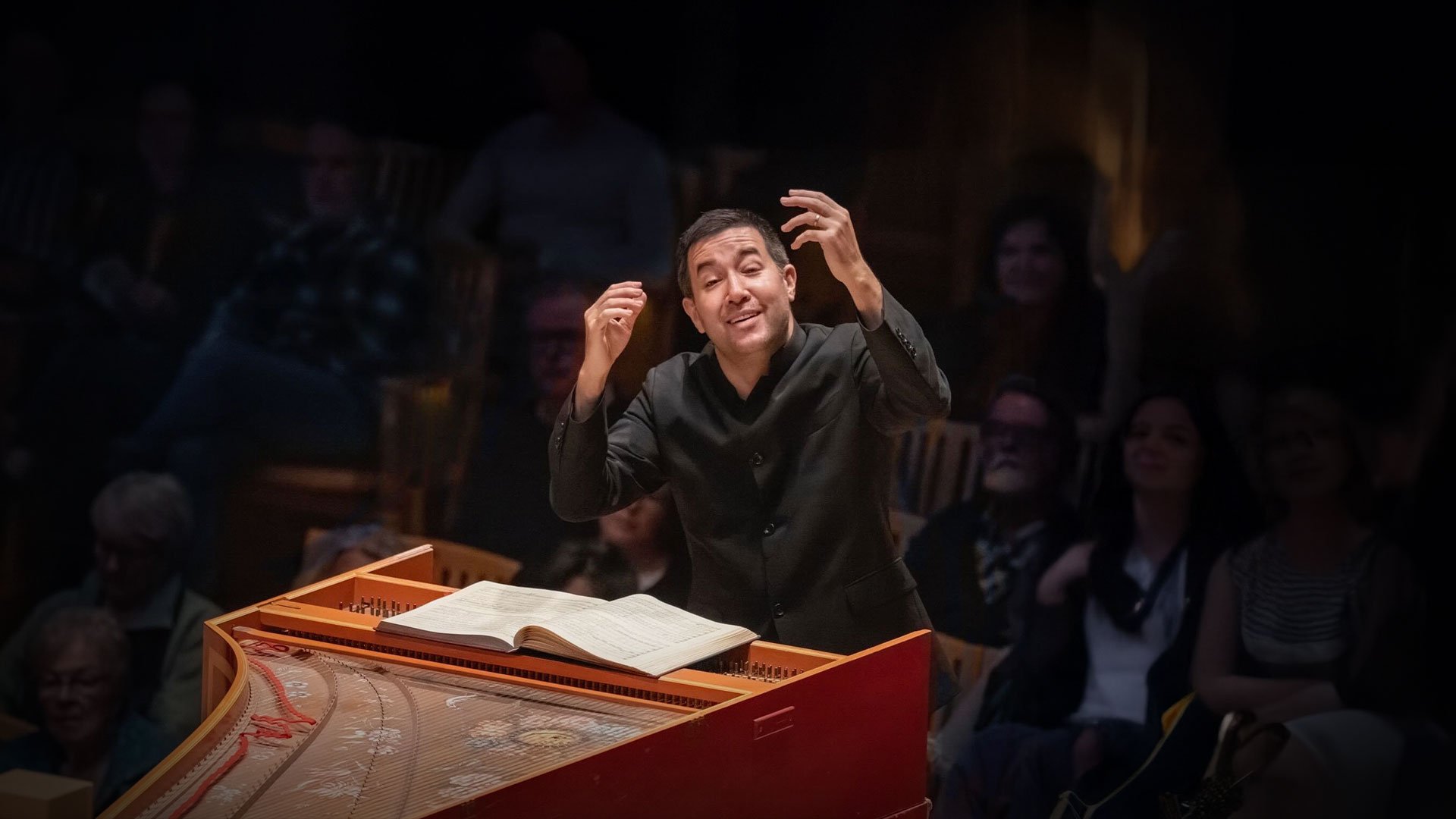 Conductor leading orchestra with sheet music on piano.