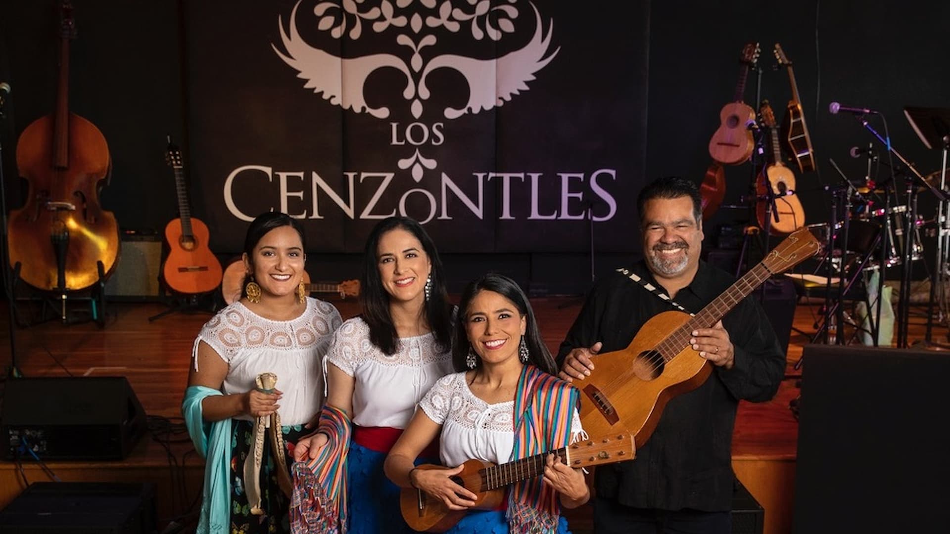 Musicians with instruments on stage, smiling.