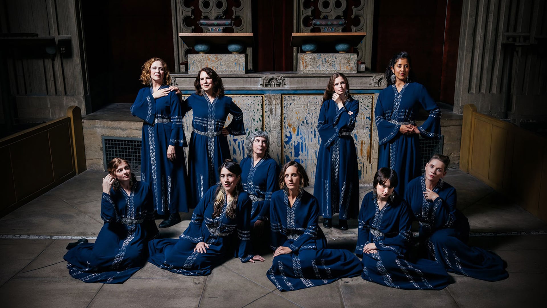 Nine women in blue dresses in ornate hall