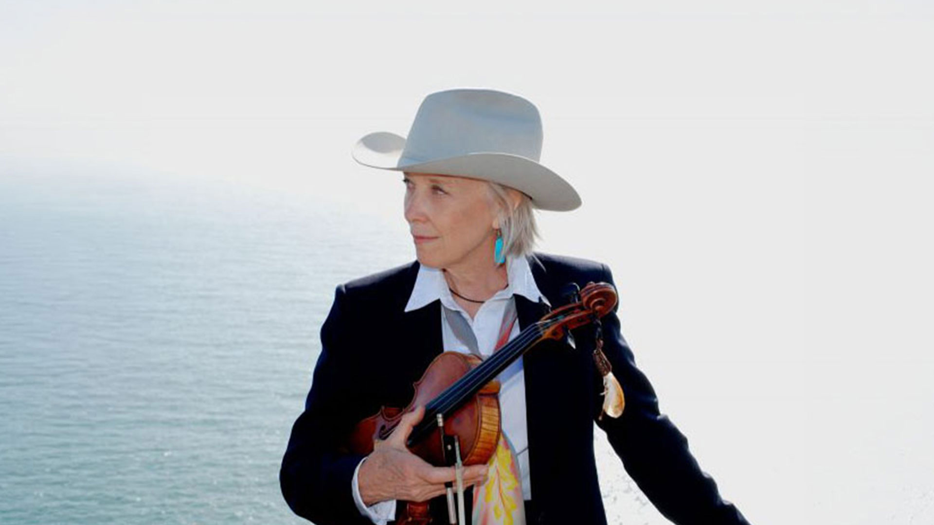 Woman in cowboy hat holding violin by ocean