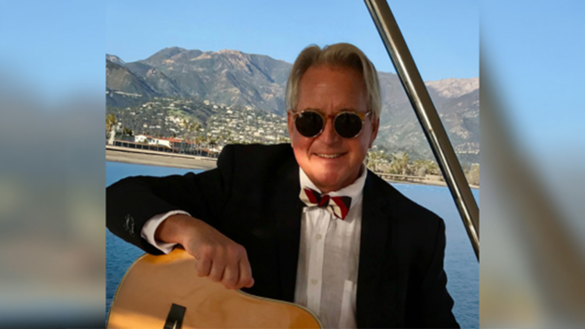 Man in suit holding guitar on boat