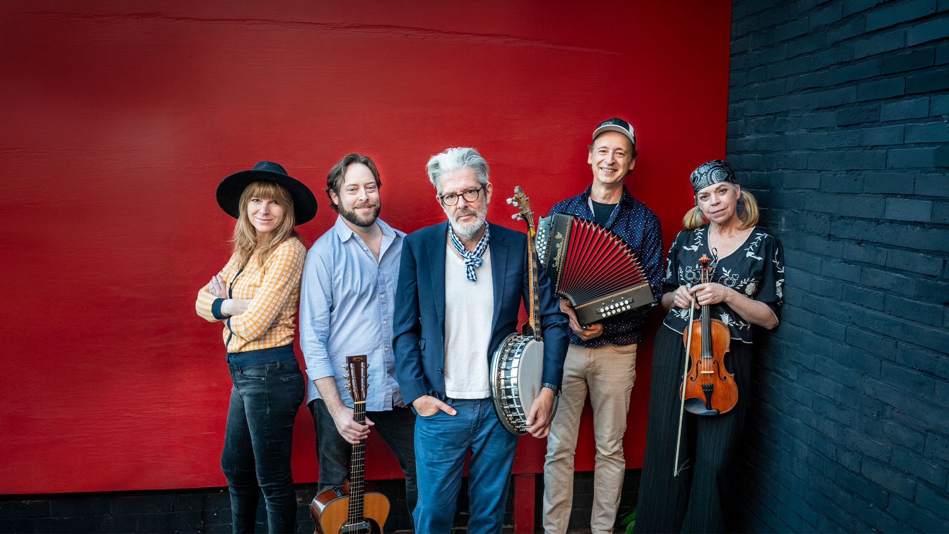 Five musicians with instruments against red wall