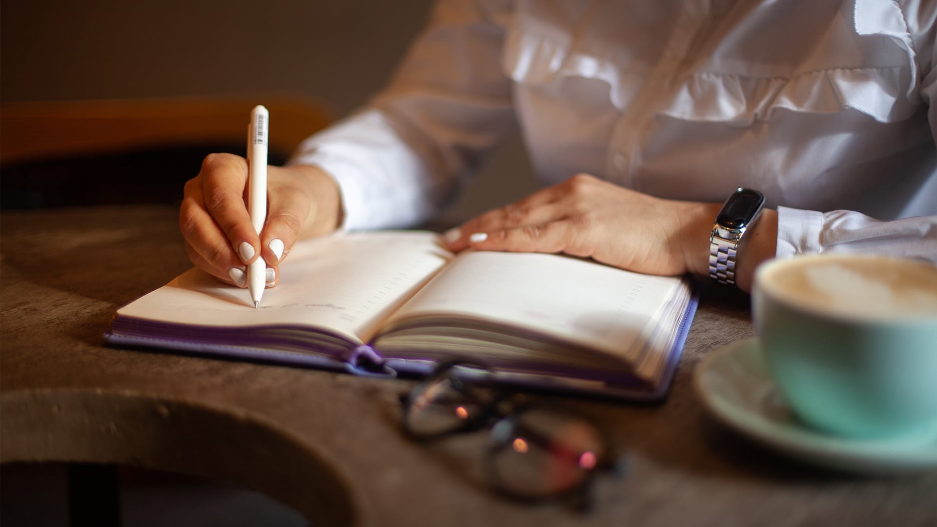 Person writing in planner beside coffee at wooden table