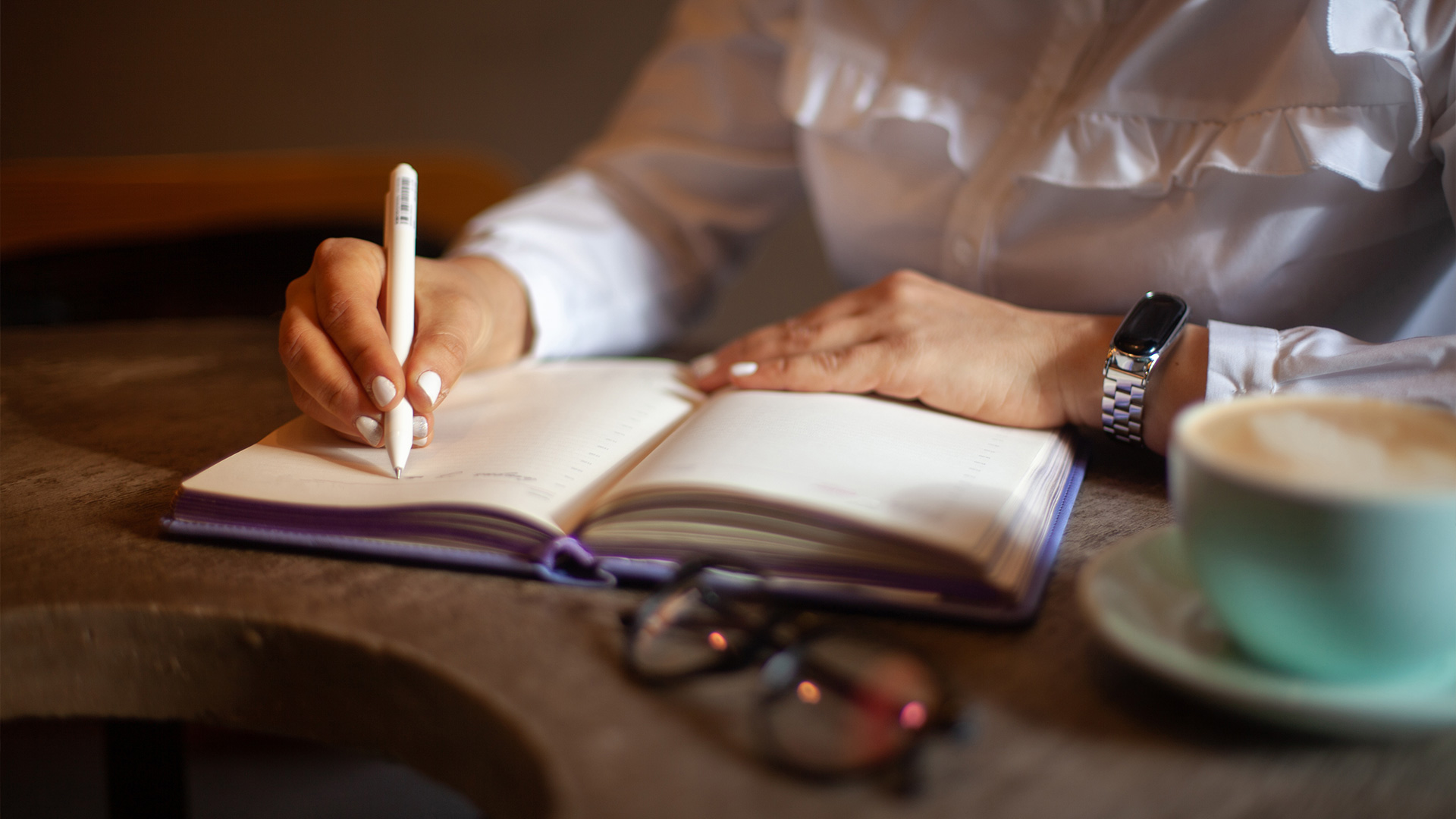 Person writing in planner beside coffee at wooden table
