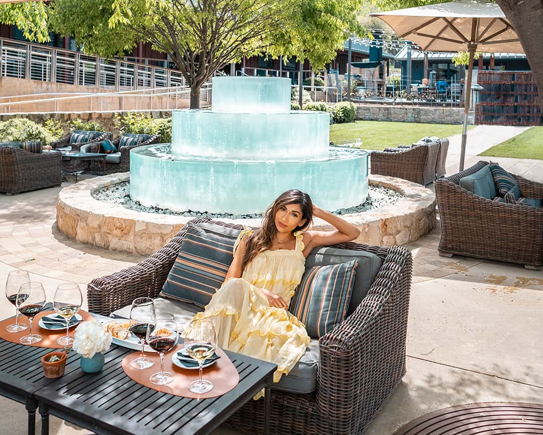 Woman relaxing outdoors by a fountain and table.