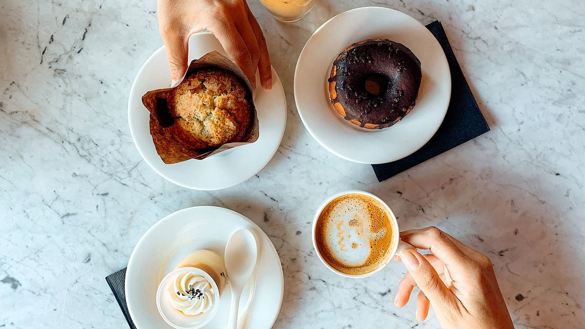 Coffee with muffin, donut, and dessert on marble table.