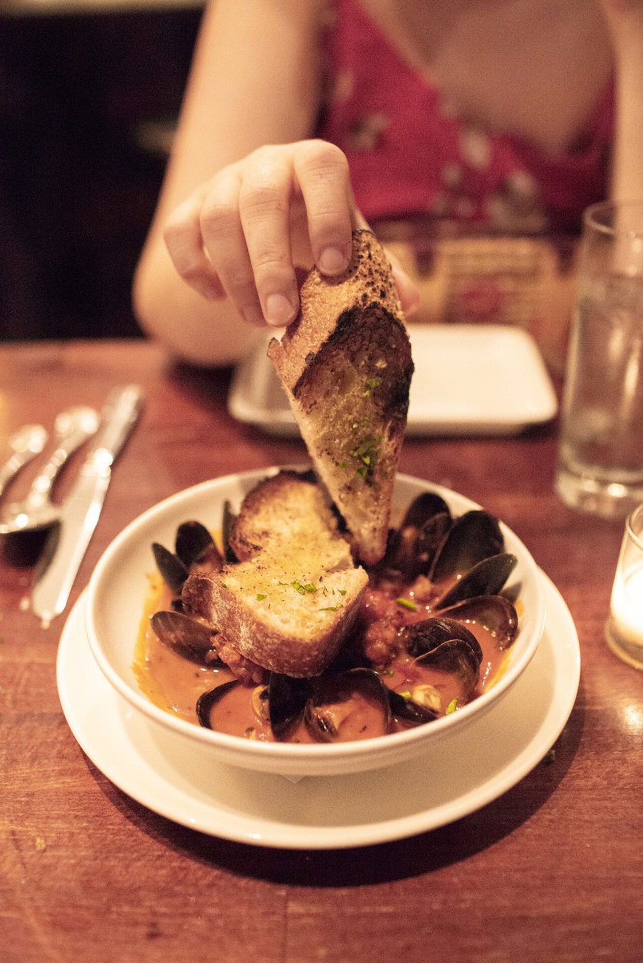 Person dipping bread into seafood soup.