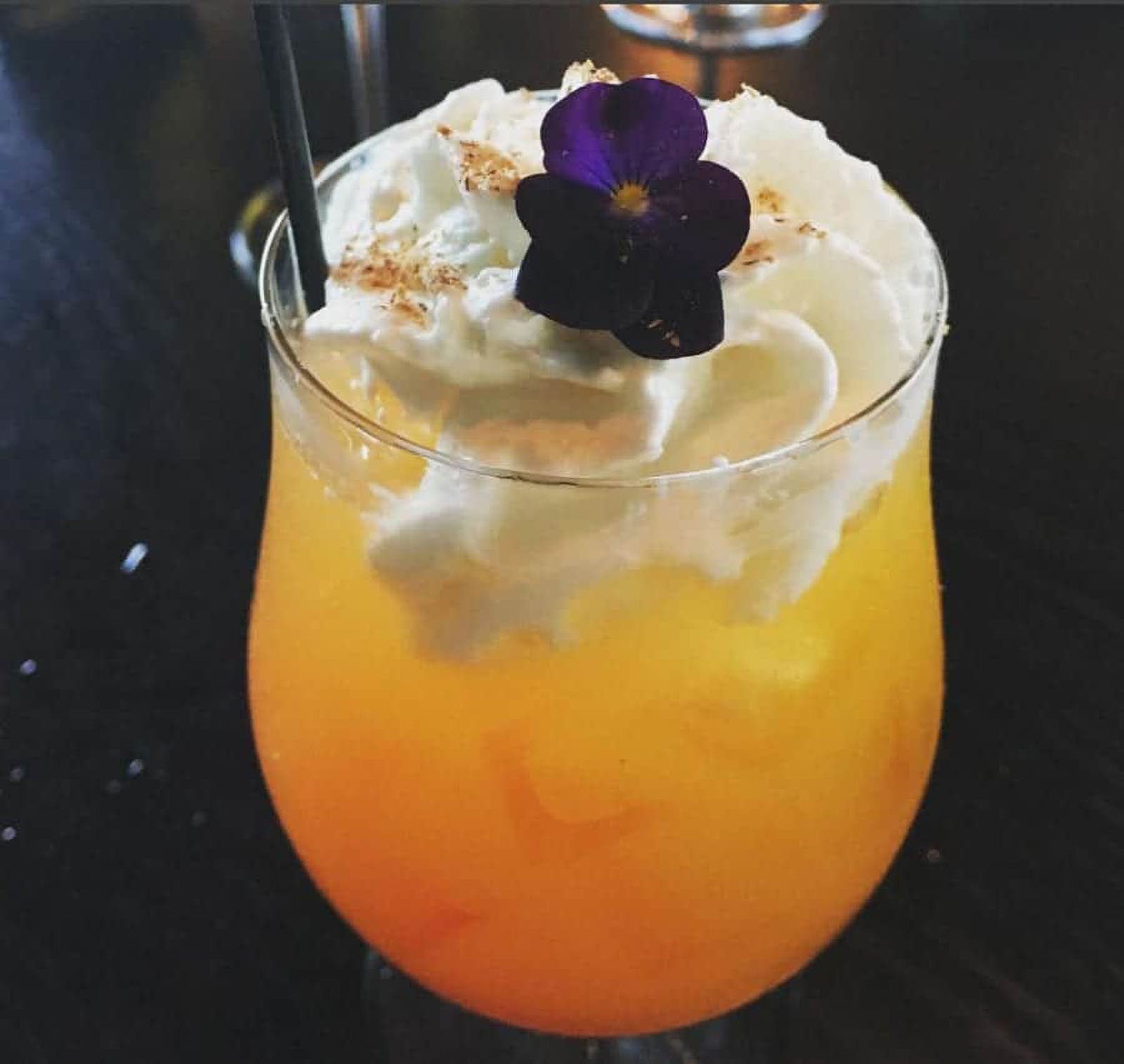 Orange cocktail with whipped cream and flower garnish.