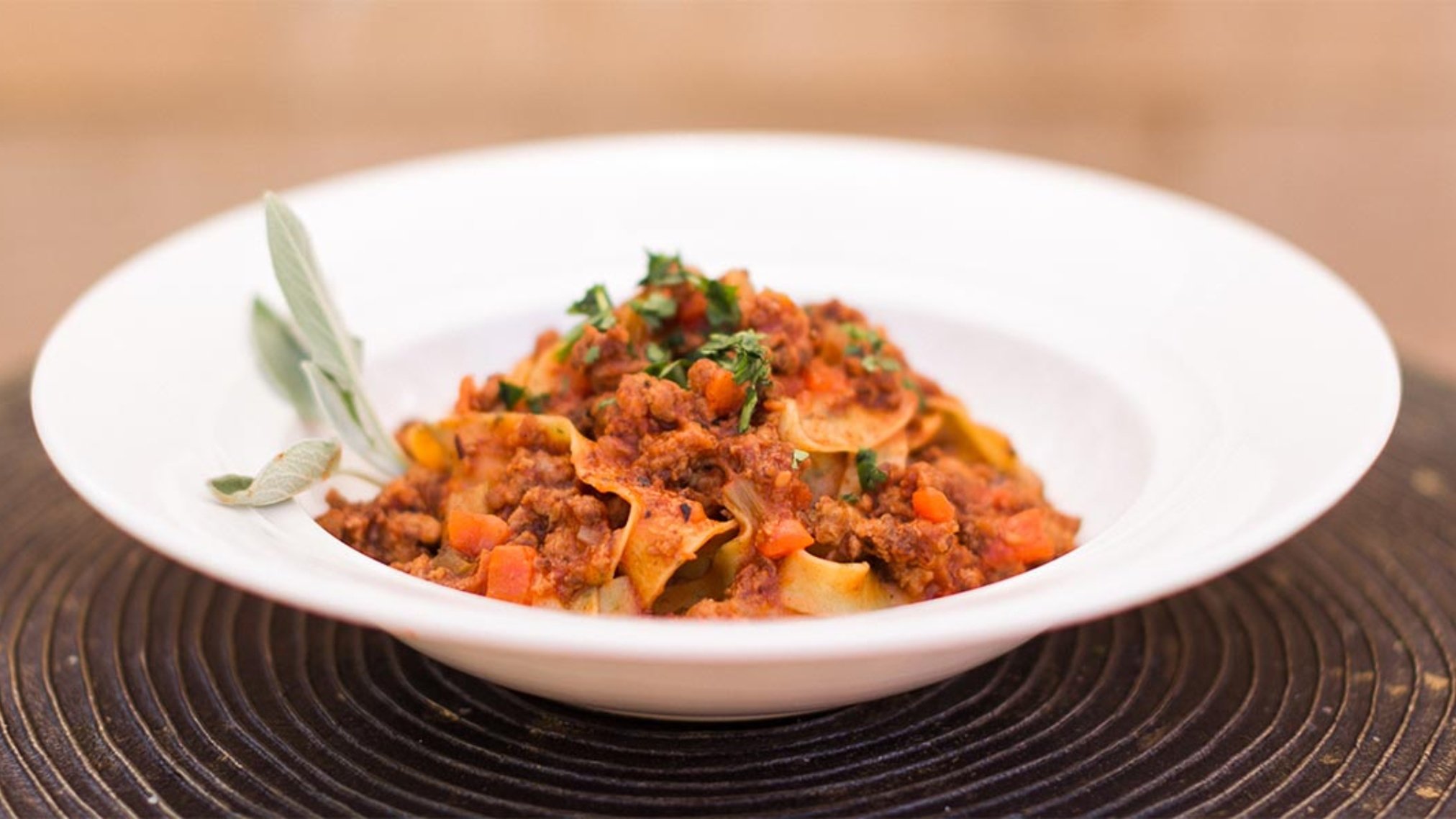 Bowl of pasta with meat sauce and herbs.