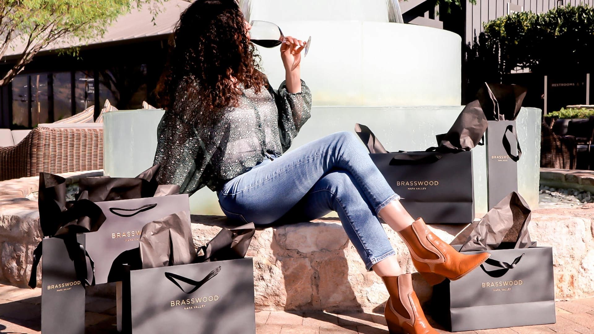 Woman drinking wine with Brasswood shopping bags.