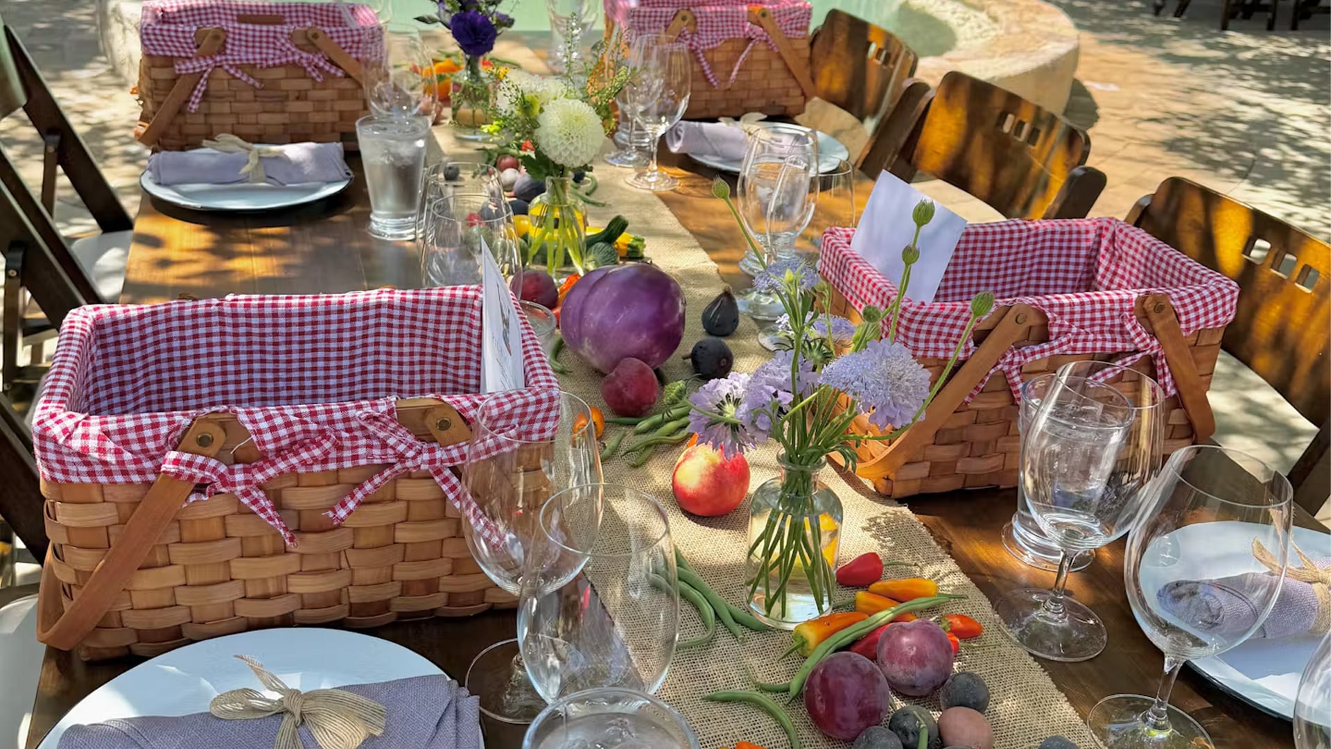 Outdoor table set with picnic baskets, flowers, and vegetables