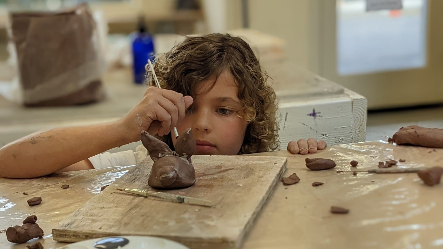 Child sculpting clay on wooden board.