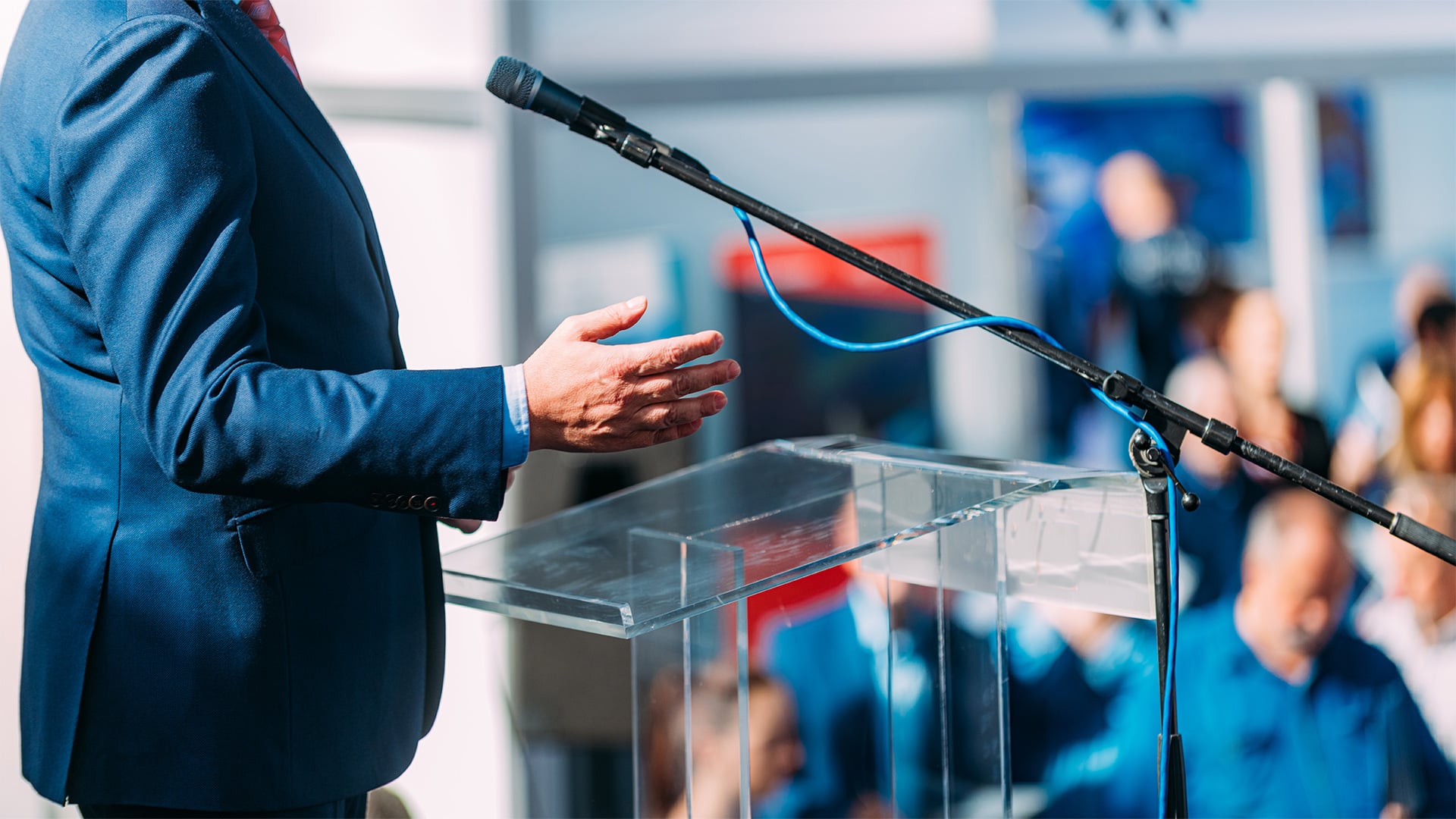 Speaker gesturing beside a clear podium and microphone