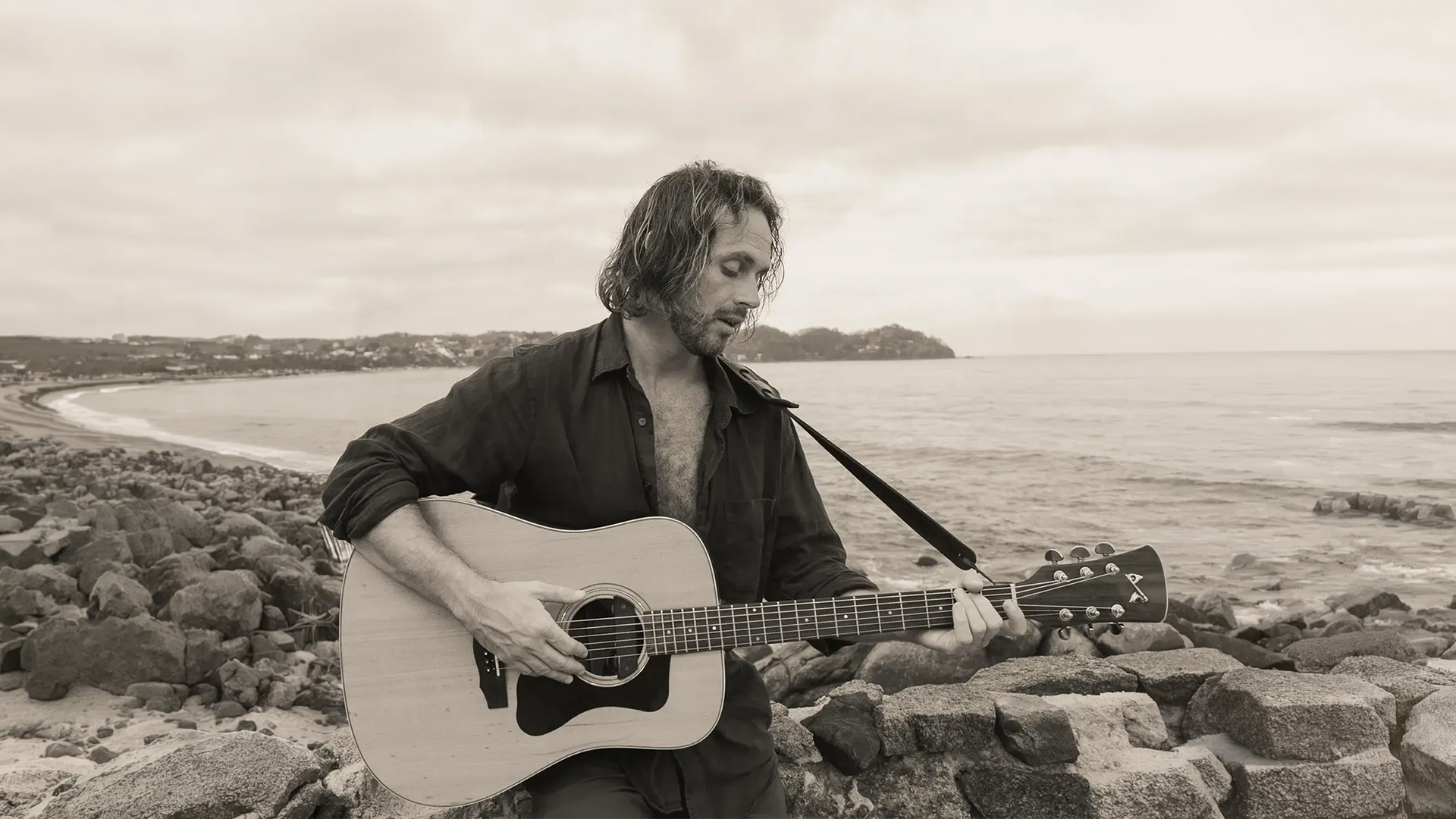 Man playing acoustic guitar on rocky shoreline