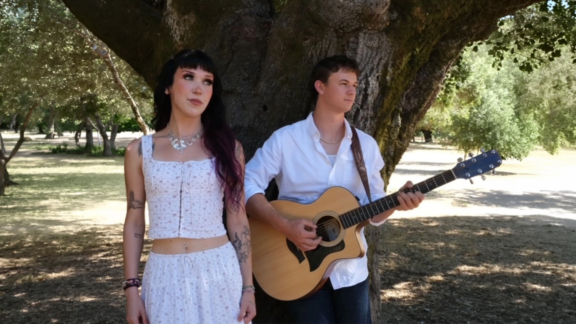 Couple under tree with acoustic guitar outdoors