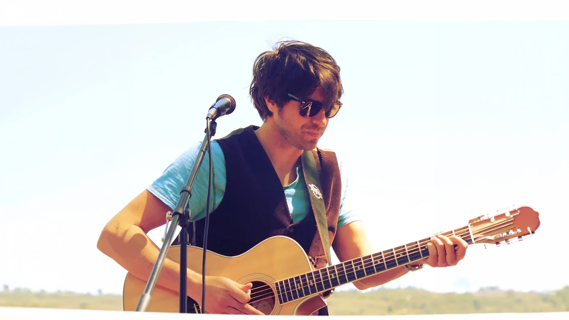 Man playing acoustic guitar outdoors with microphone