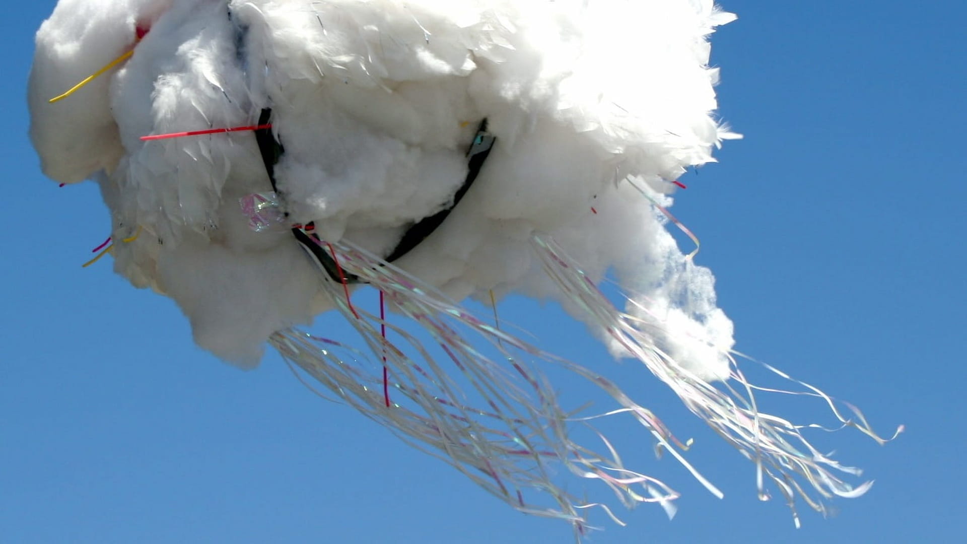 Cloud-shaped kite with colorful streamers flying high.