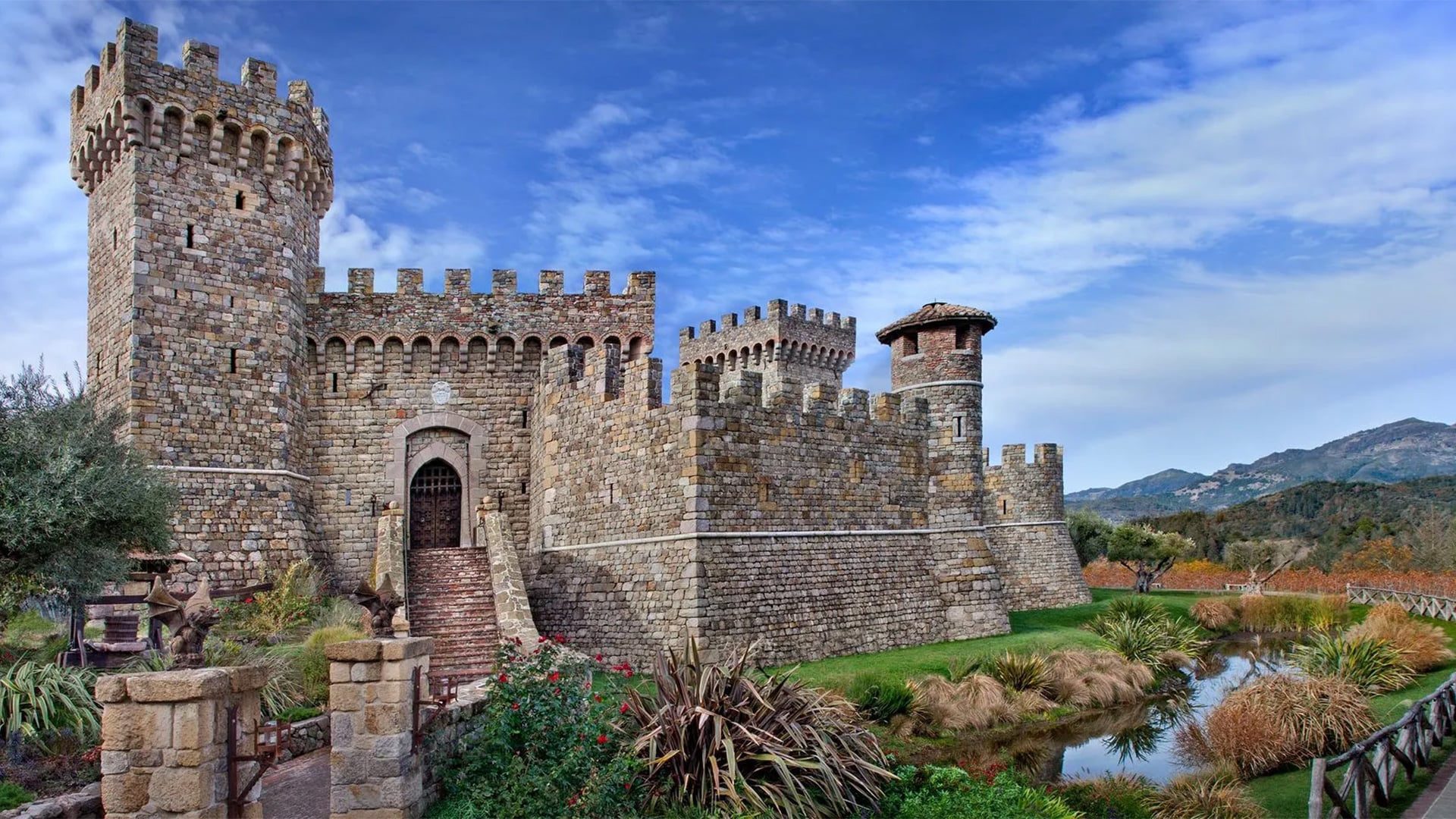 Stone castle with towers beside landscaped pond and mountains