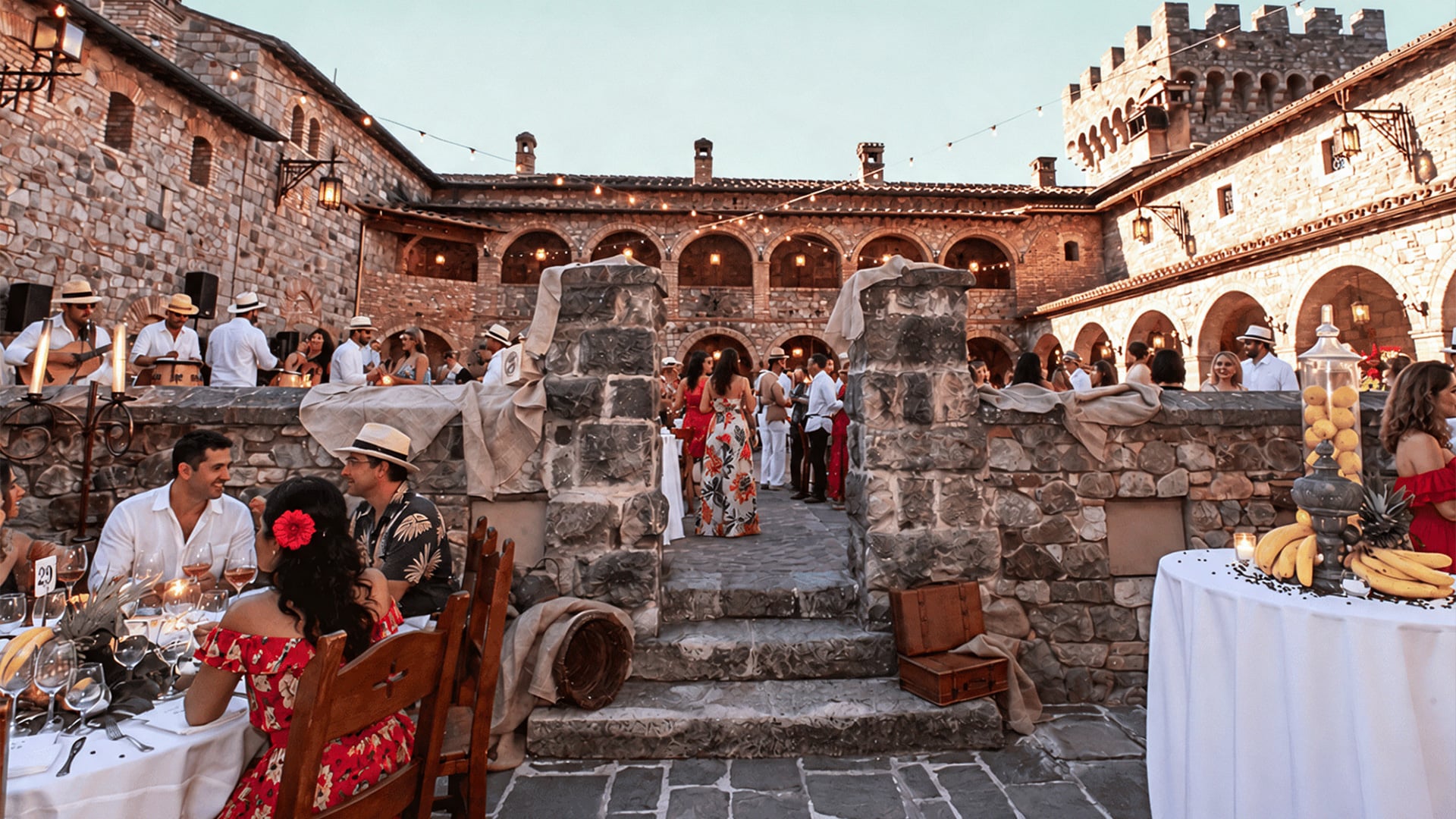 Guests gather at candlelit banquet in historic stone courtyard.