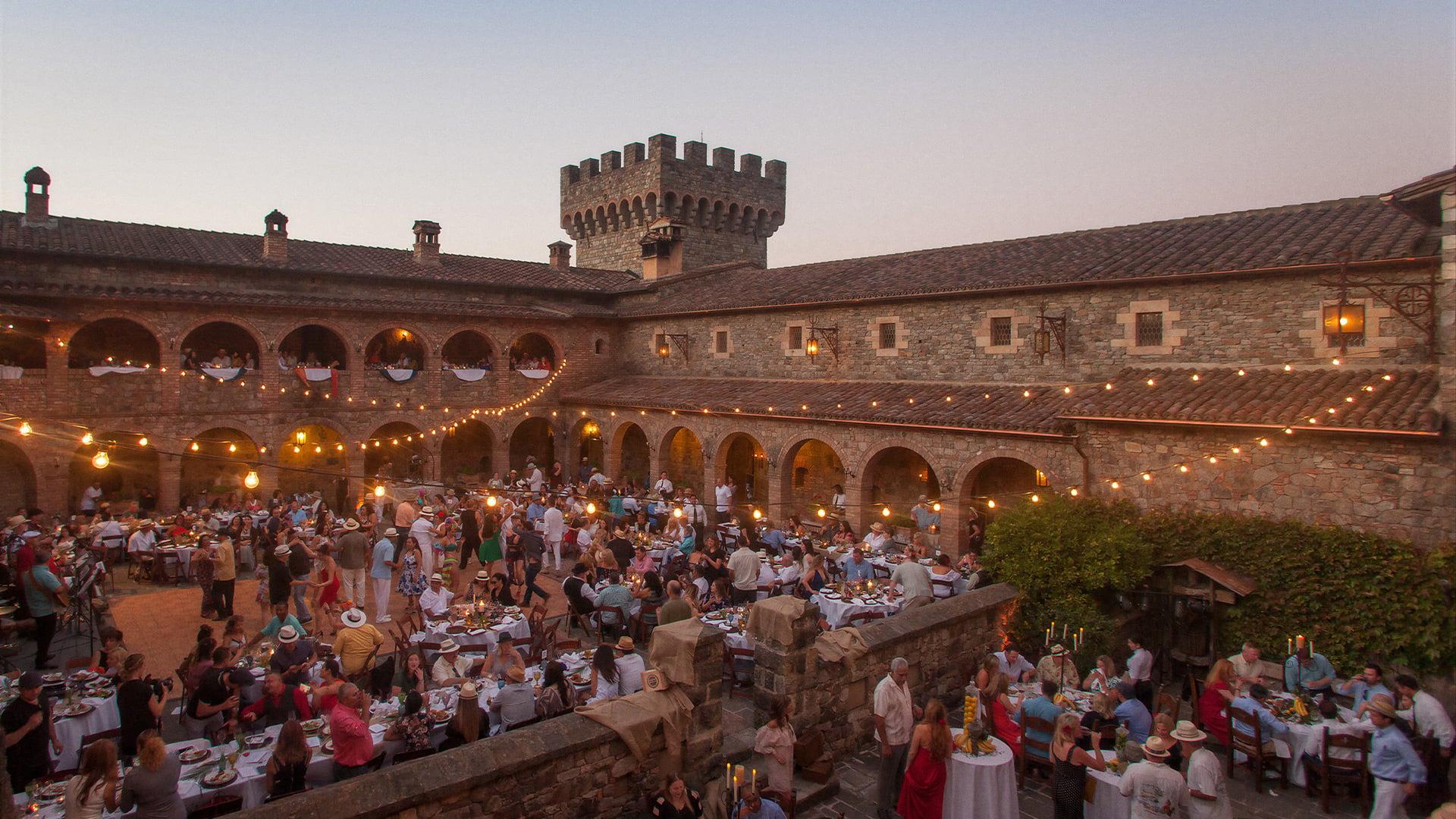 Guests dine in a candlelit medieval castle courtyard