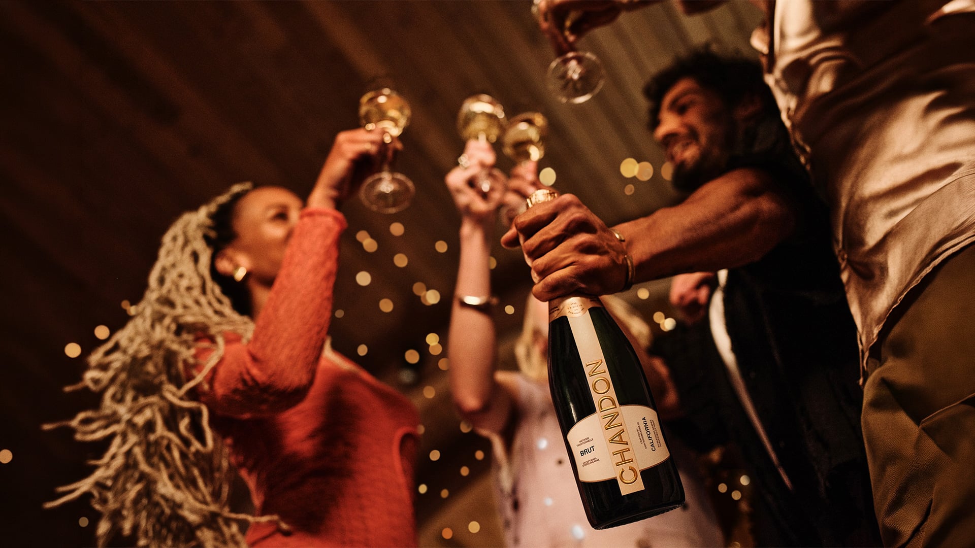 Friends raise champagne glasses as a bottle is opened