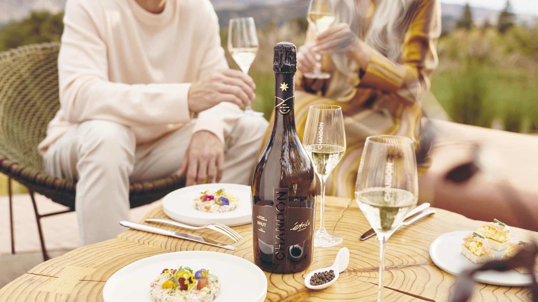 Chandon bottle with glasses and plates on table.