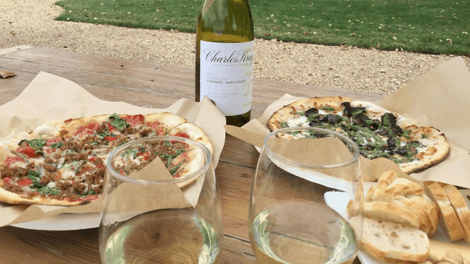 Pizza and wine on outdoor picnic table.