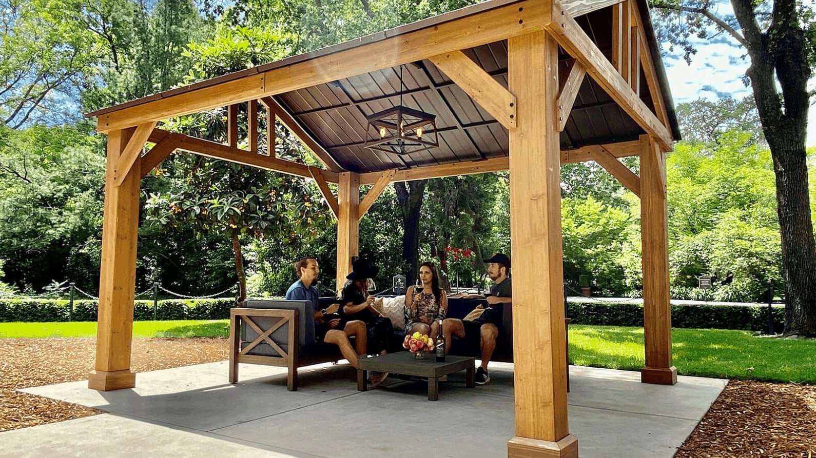 People sitting under a wooden pavilion in a park.