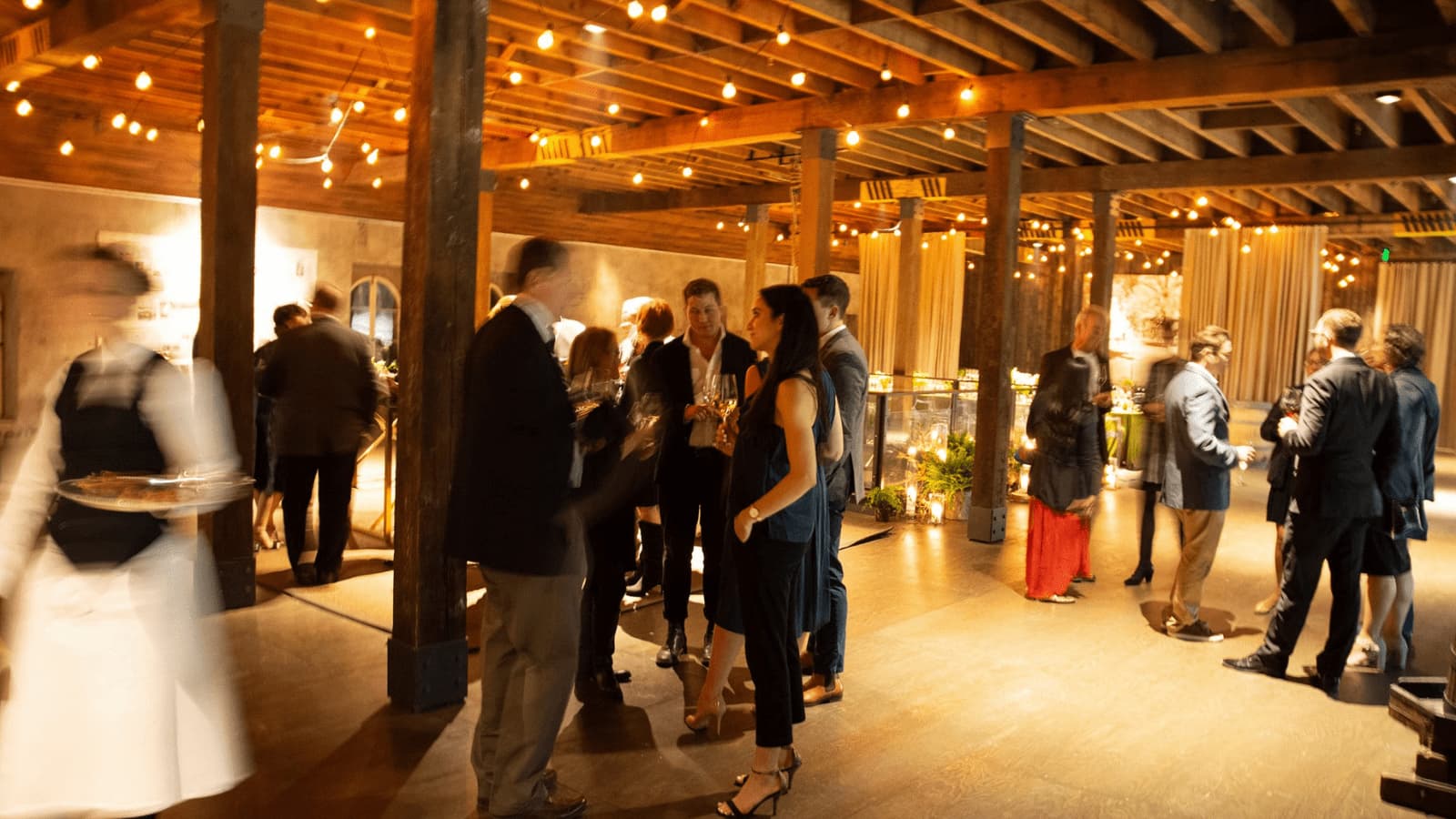 People mingling at a social event with string lights.