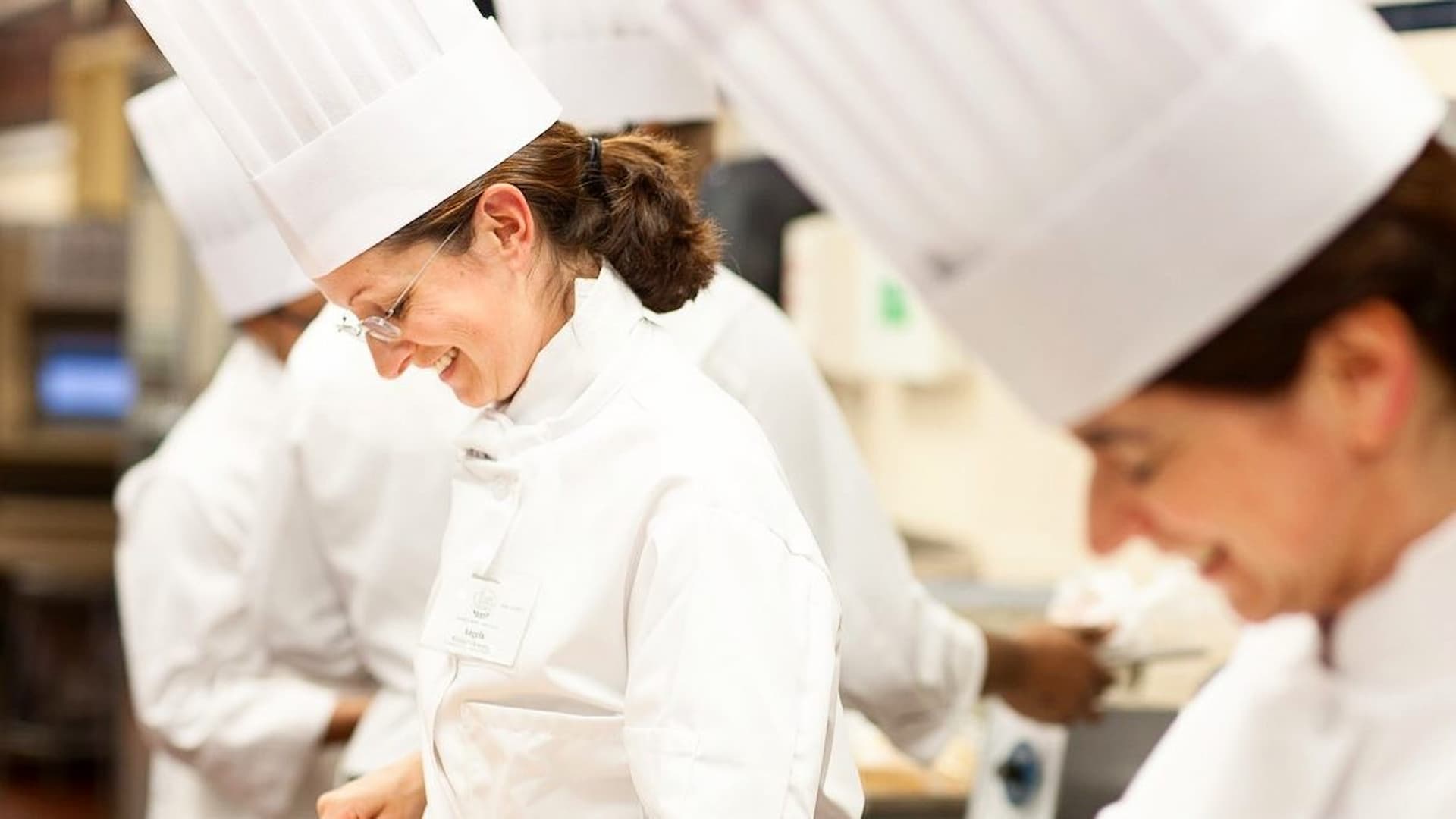 Smiling chefs working in kitchen, wearing white uniforms.