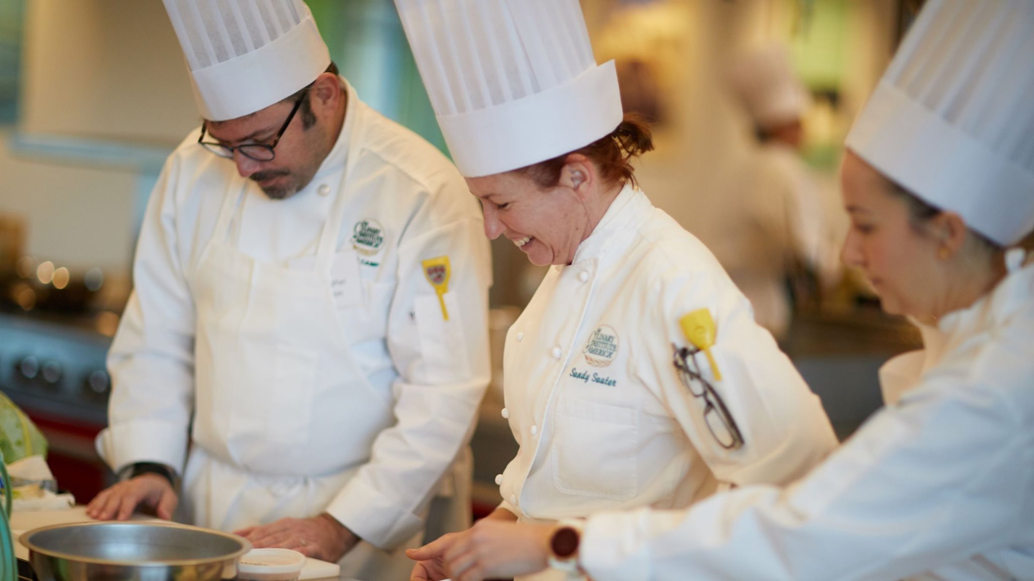 Chefs cooking together in a kitchen, wearing uniforms.