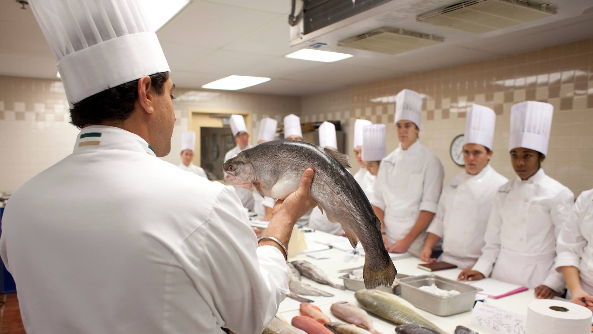 Chef teaching students while holding fresh fish