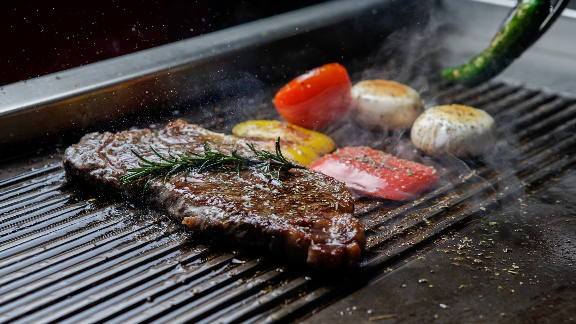 Sizzling steak with rosemary and vegetables on grill