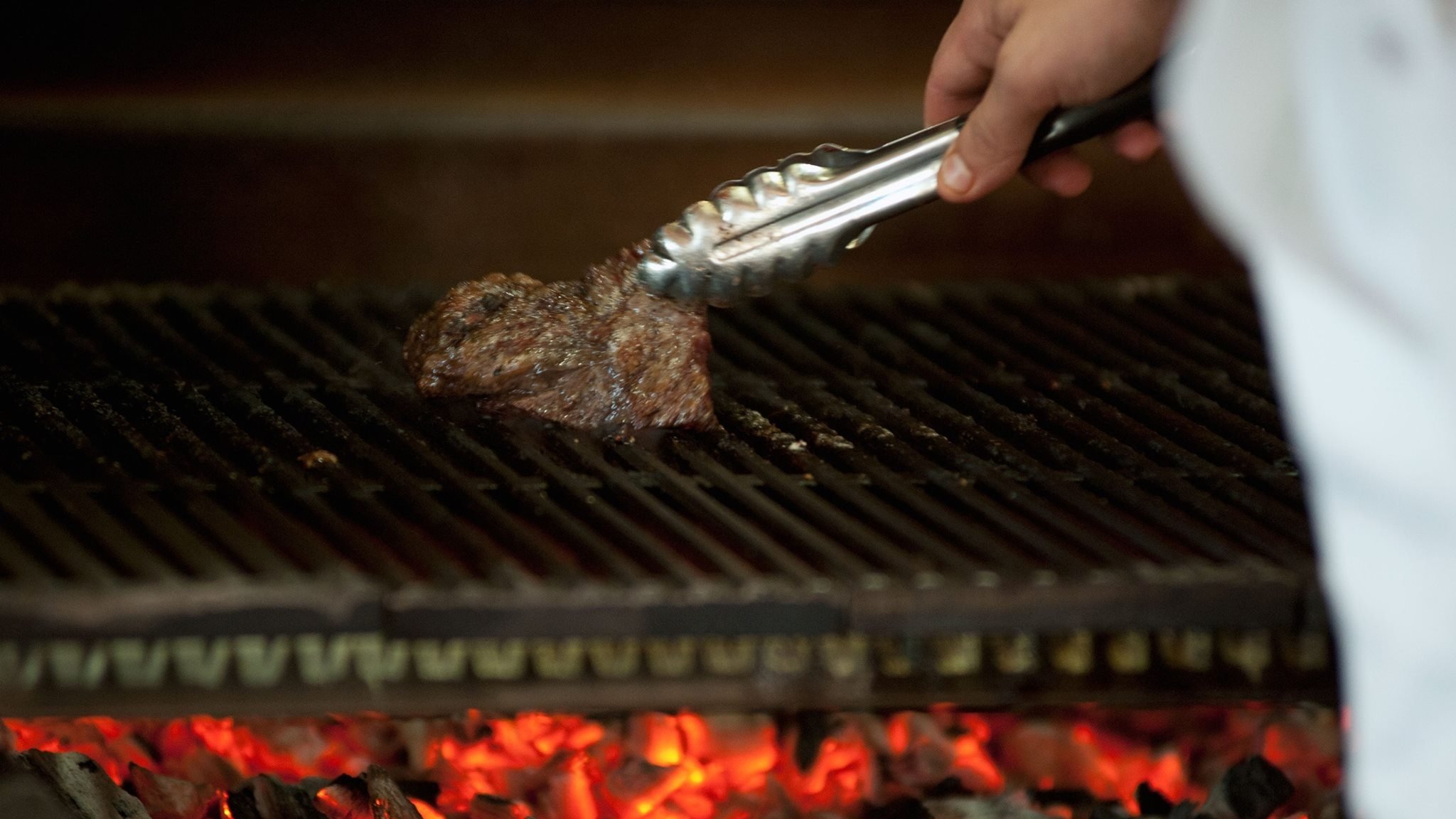 Grilling steak over hot coals with tongs.
