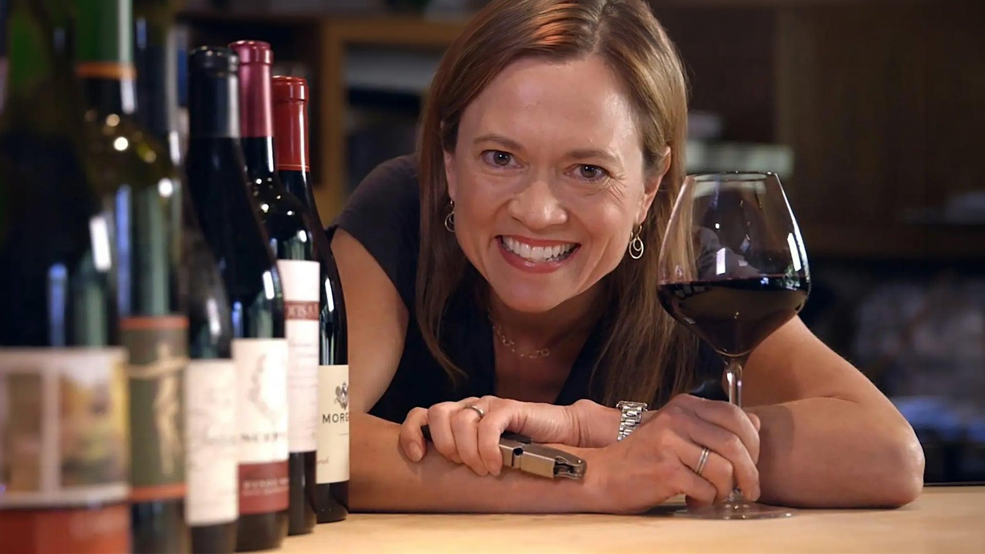 Smiling woman holding red wine beside bottles
