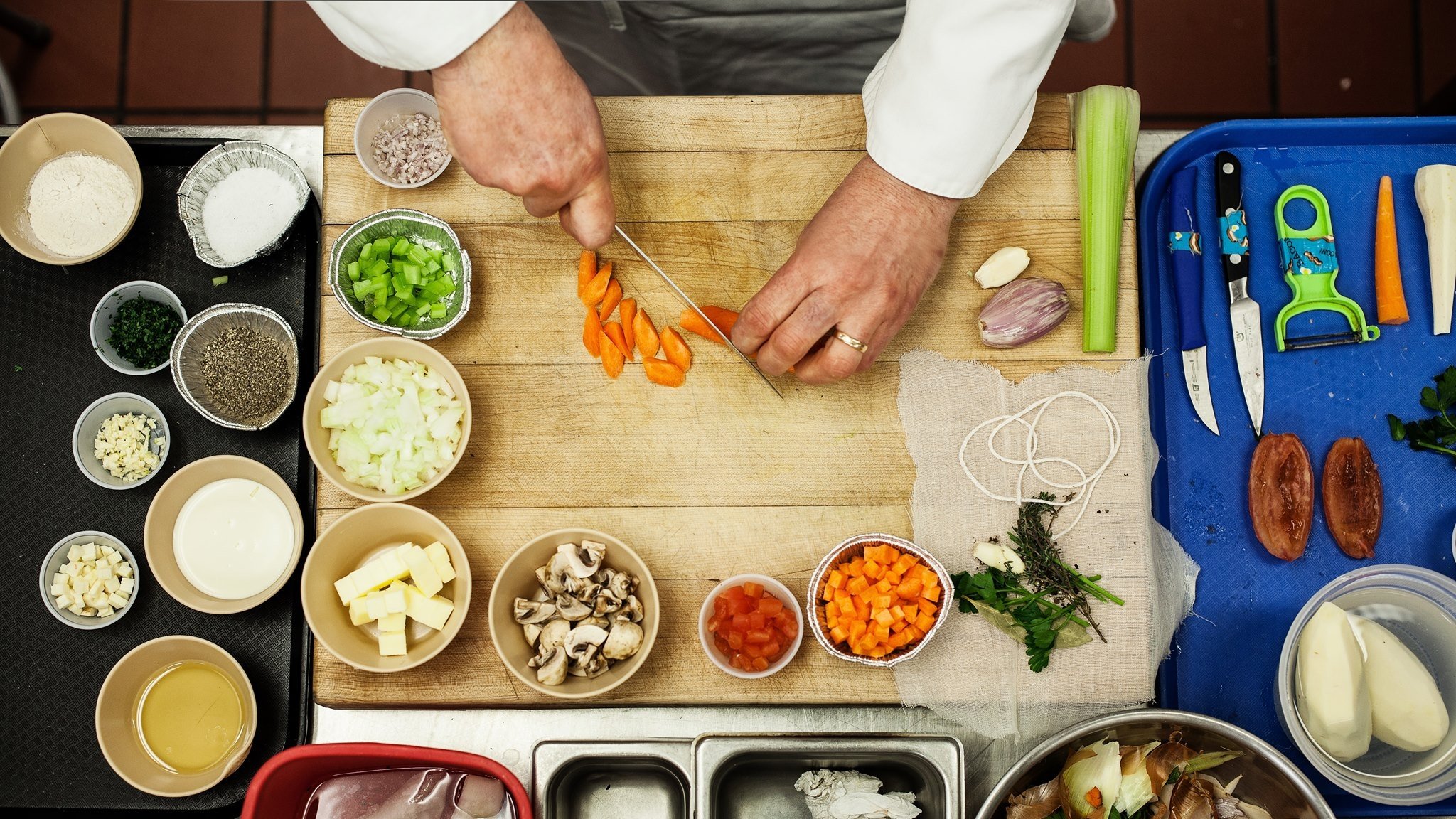Chef chopping carrots with assorted ingredients around.