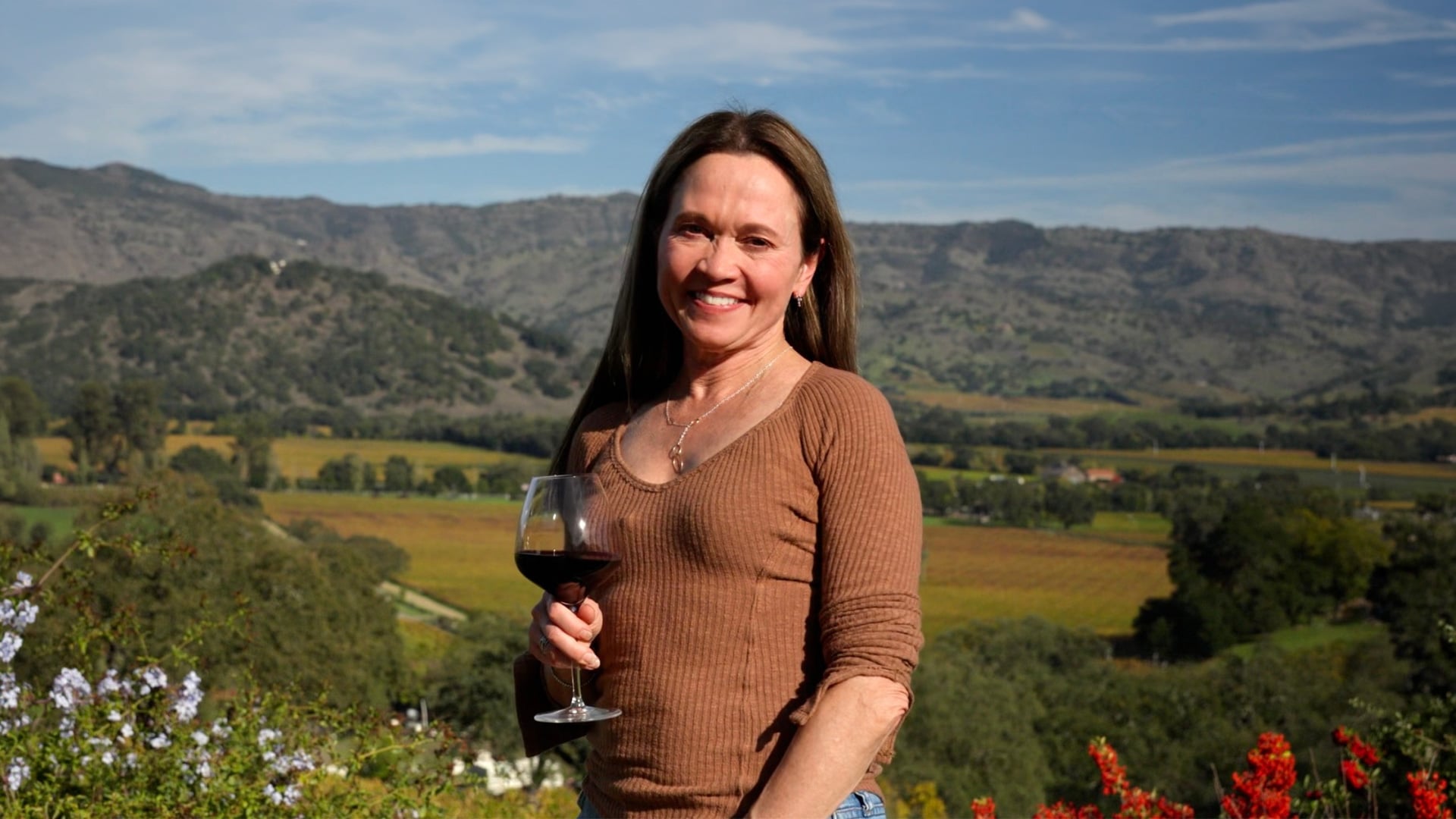 Woman holding red wine overlooking a vineyard valley