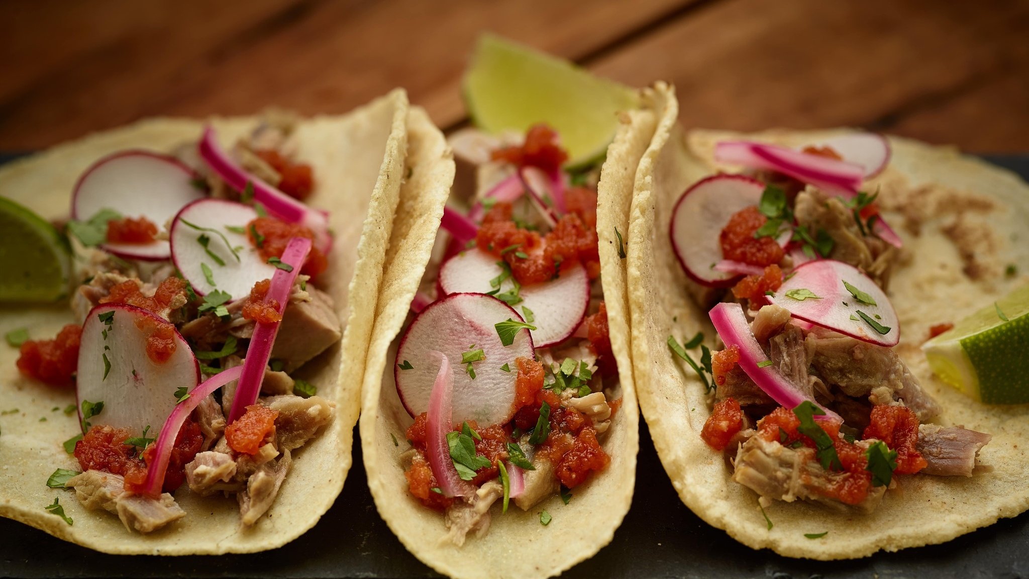 Three tacos with radishes and lime on a plate.