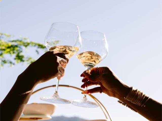 Two people clink rosé wine glasses outdoors