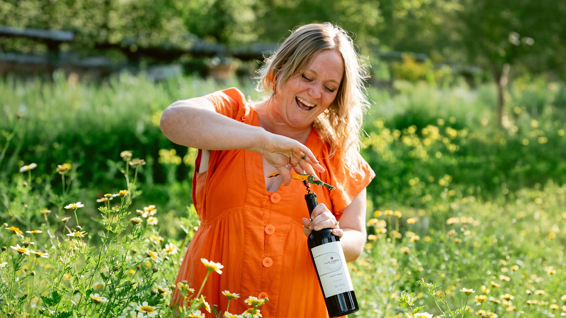 Woman opening wine bottle in sunny wildflower field