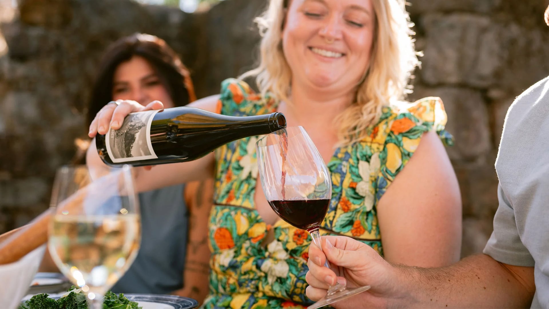 Woman pours red wine during outdoor dinner