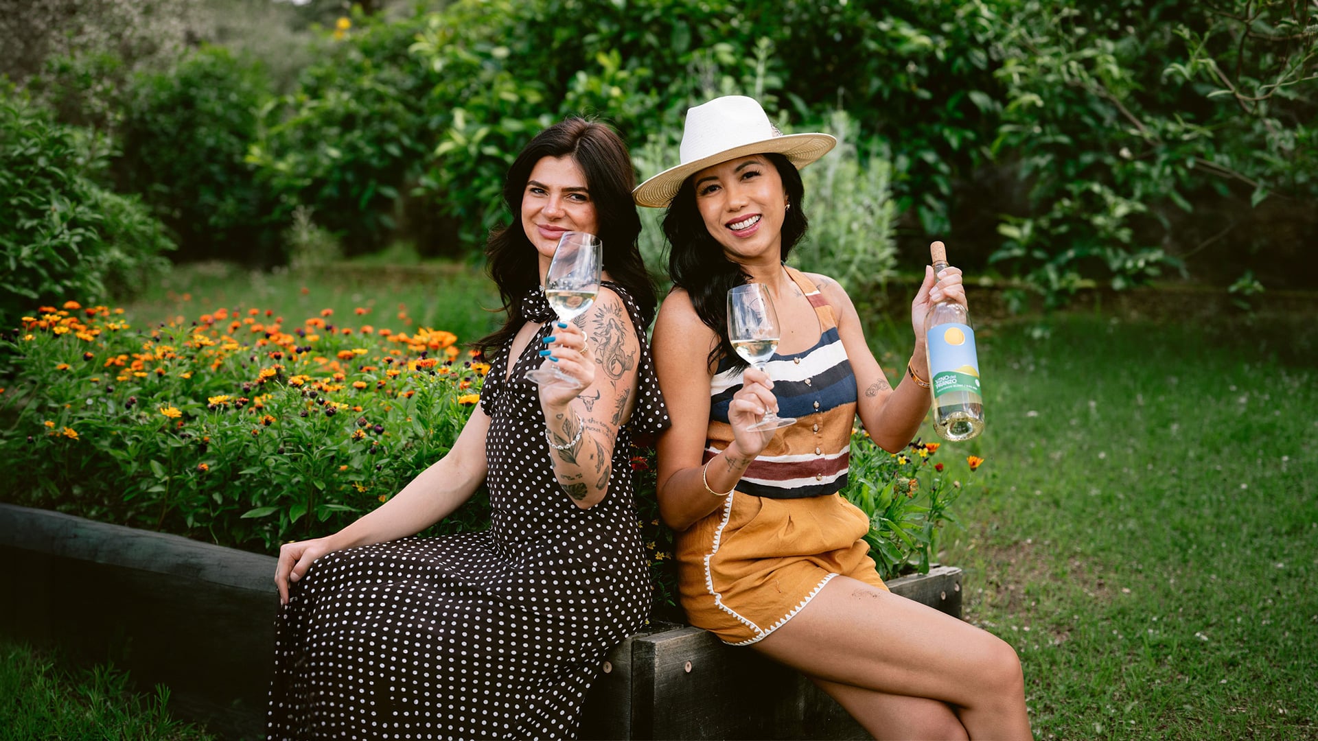Two women toast with wine in a flower garden.