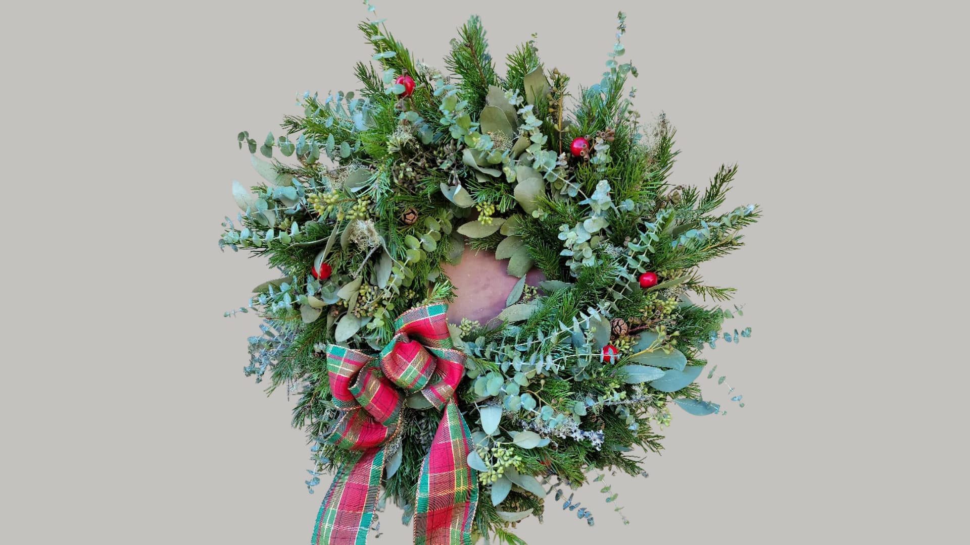 Festive wreath with greenery and red plaid bow.